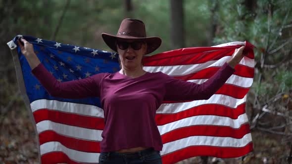 Woman whipping American flag over head and wrapping it around her and giving the Victory sign with h alt