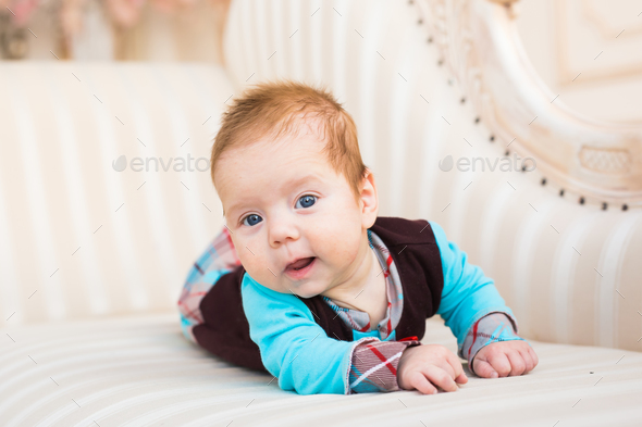 Close-up portrait of baby boy with red hair and blue eyes. Newborn child  lyling in couch. Stock Photo by Satura_