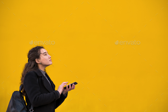 An Asian girl in a black coat and a phone with her hand walks