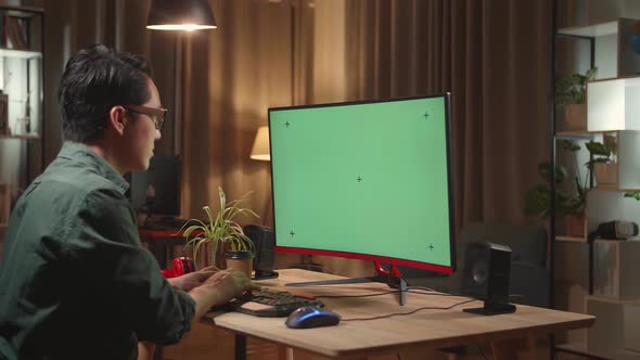 Asian Male Works With Mock Up Green Screen Computer Display. He Works At Night alt