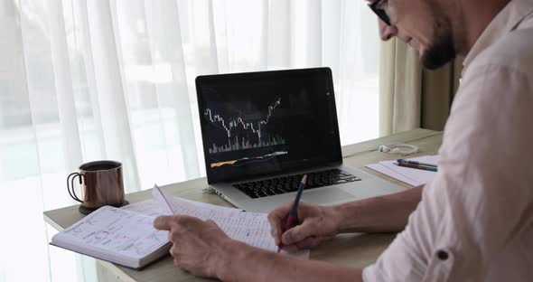 Crop Bearded Analyst Making Notes on a Clipboard Looking on a Trading Chart alt