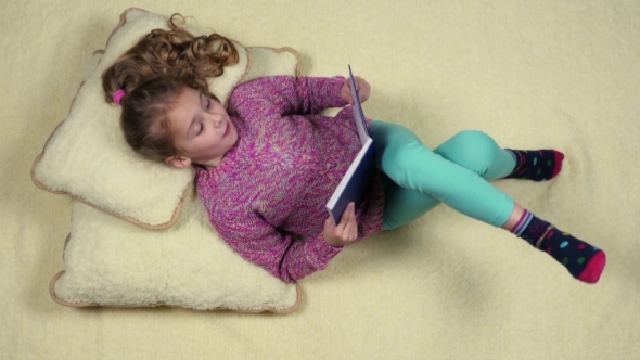Funny Little Girl Lying on the Couch Reading a Book. Top View