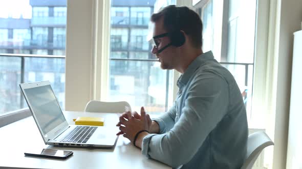 Confident Male Worker Sitting at the Desk with a Laptop and Working Remotely alt