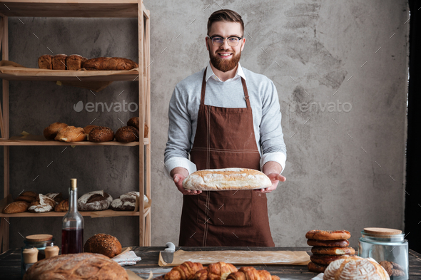 Cheerful young man baker standing at bakery holding bread Stock Photo by  vadymvdrobot