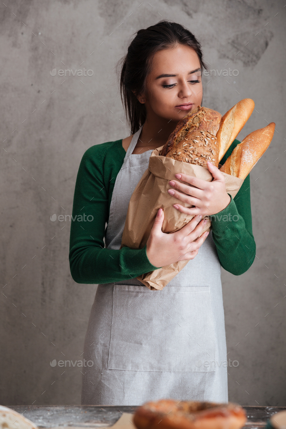 Young happy lady baker standing and holding bread. - Stock Photo - Images