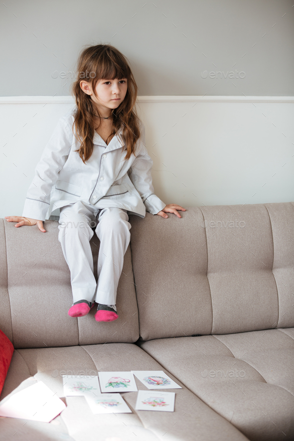 Little girl sitting on couch in living room Stock Photo by vadymvdrobot