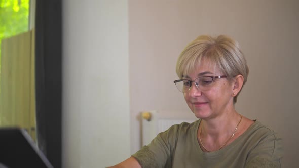 Blonde Smiling Adult Women in the Glasses is Learning New Information on Laptop