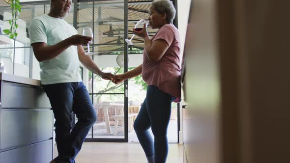 Happy african american senior couple drinking vine in kitchen alt