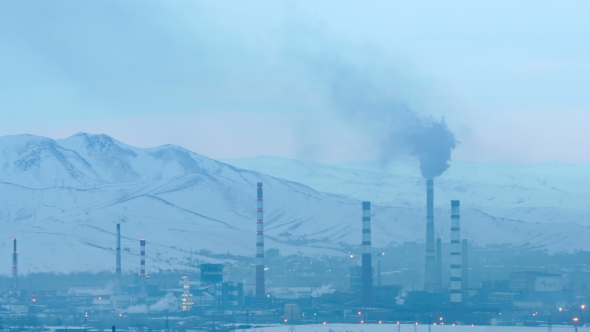 Operating Factory with Smoking Chimneys Against Snow-capped Mountains Background