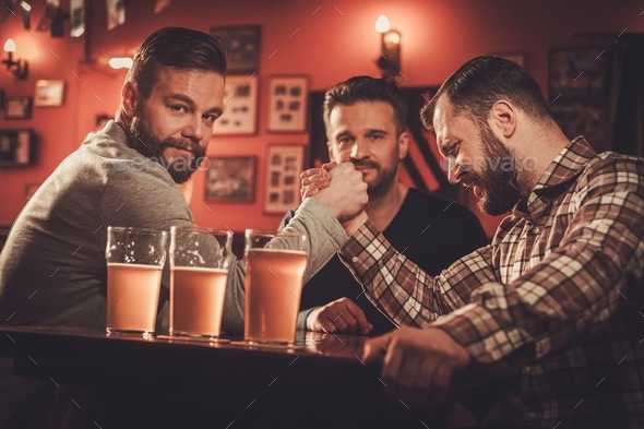 Cheerful old friends having arm wrestling challenge in a pub.