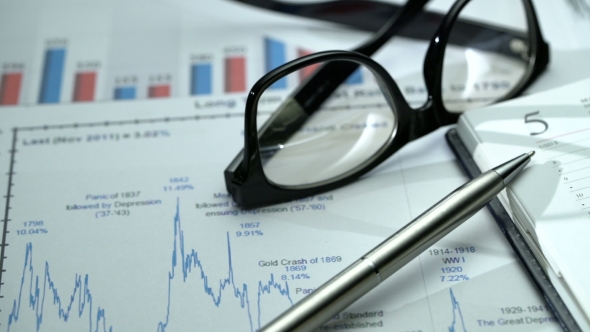 Tracking  Shot of Office Desk with Business Graphics, Glasses, Pen and Notebook.