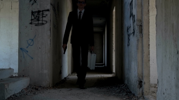 A Man with a Gun and a Case in His Hand is Walking Along the Corridor of an Abandoned Building alt