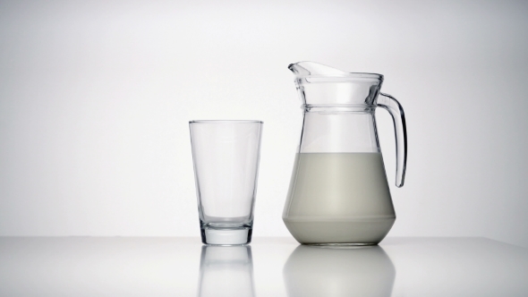 Jug of Milk and an Empty Transparent Glass Standing on White Surface