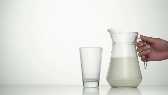 Female Hand Taking Jug of Milk and Pouring Into Empty Glass