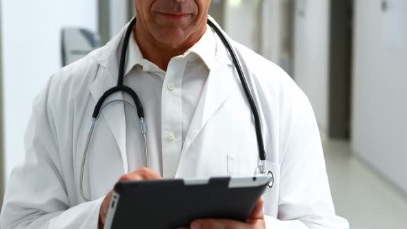 Smiling doctor using digital tablet in corridor alt
