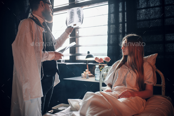 Male doctor looking at x-ray picture of sick woman - Stock Photo - Images