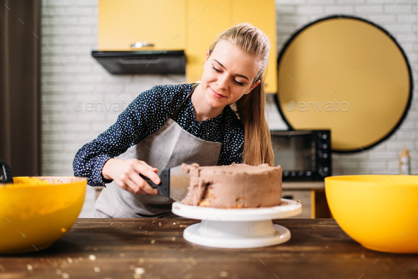 Woman cook smears baked cake with chocolate cream - Stock Photo - Images