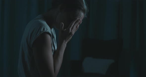 Exhausted woman sitting in bed and suffering from insomnia, she is touching her face