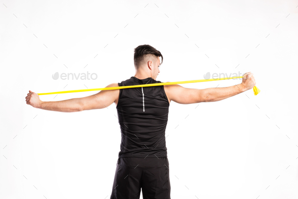 Handsome fitness man working out with rubber band, studio shot.