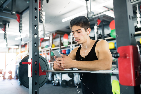 Hispanic man in gym resting, holding smart phone,listening music