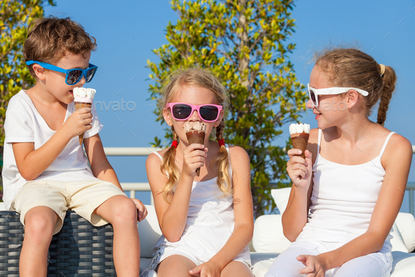 three happy children eating ice cream near swimming pool at the Stock Photo by altanaka