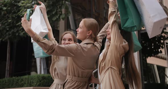 Three Happy Girls Taking Selfies and Raising Up Shopping Bags While Standing at Street. Pretty alt