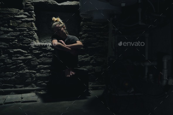 depressed anxious woman sitting in a dark corner of a basement