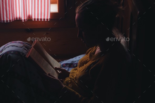 woman reading book in a bed, wooden cottage interior