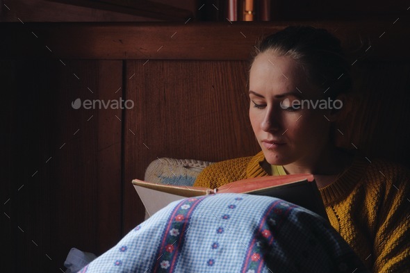 woman reading book in a bed, wooden cottage interior