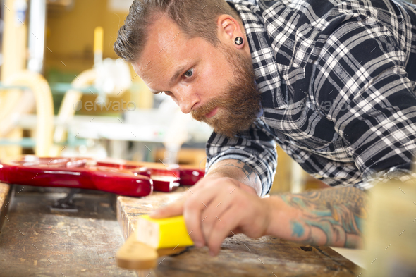 Carpenter sanding guitar neck in wood at workshop - Stock Photo - Images