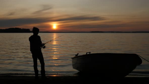 Silhouette Of Teen Boy Fishing Near Rowboat In Scenic Place At Sunset