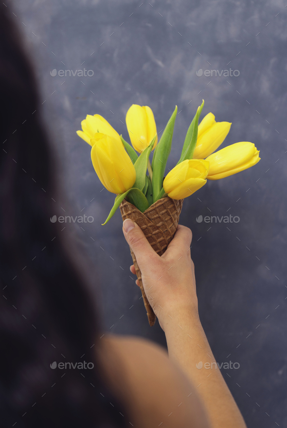 Yellow tulips in ice cream cone in girls hand on cement backgrou