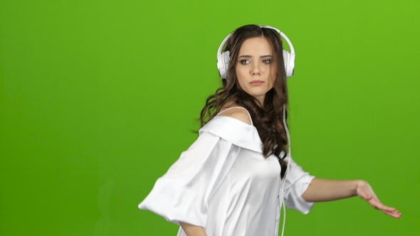Girl Listens Through the Headphones Music and Whirl Around Her. Green Screen alt