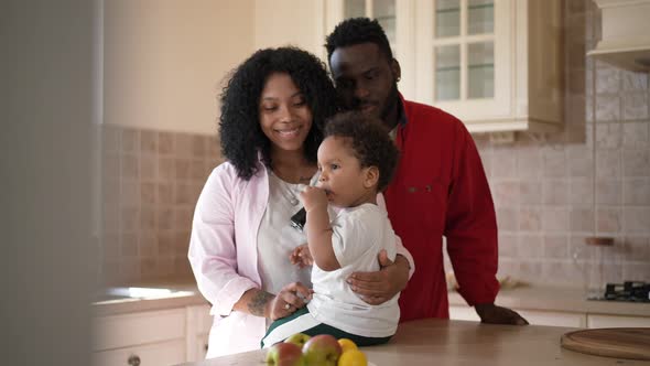 Carefree Adorable African American Toddler Boy Eating Children Food From Tube As Satisfied Father alt