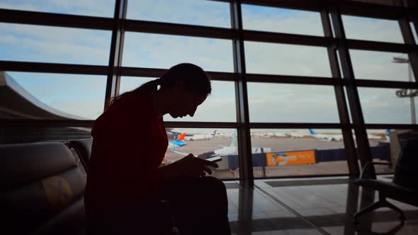 Businesswoman at Airport with Phone in Hands Against the Large Panoramic Window with Parking alt