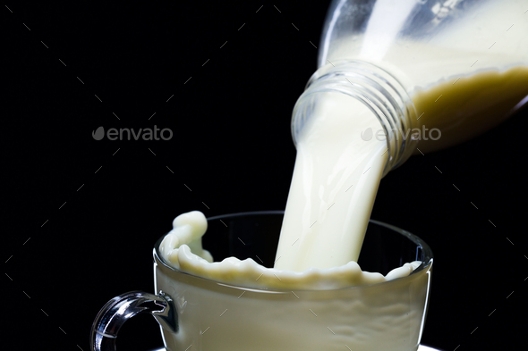 Milk pours into glass ware on a black background Stock Photo by oleghz