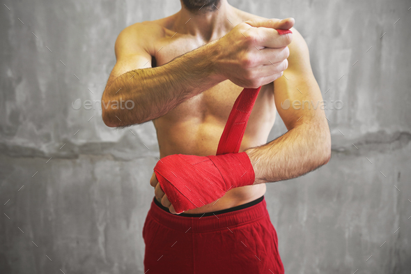 Man is wrapping hands with red boxing wraps.