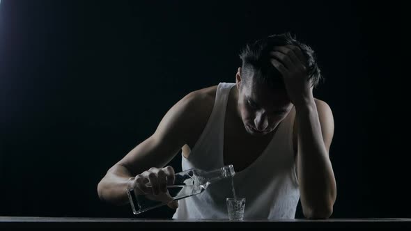 Depressed Man Drinking Alcohol Alone in a Dark Room