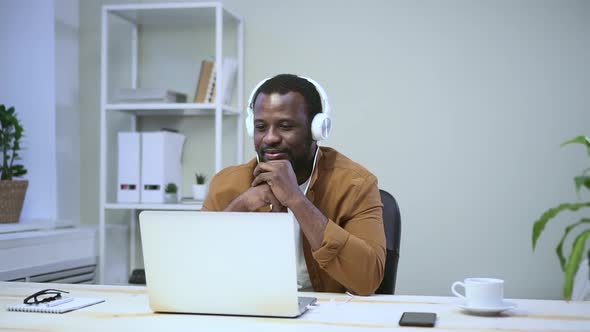 African is Chatting Online Through Headphones in Computer on Table in Room Spbas alt