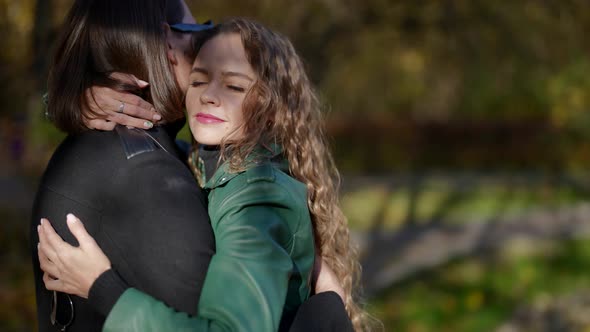 a Blonde in a Green Jacket Hugs a Man in Sunglasses in an Autumn Park on a Sunny Day alt