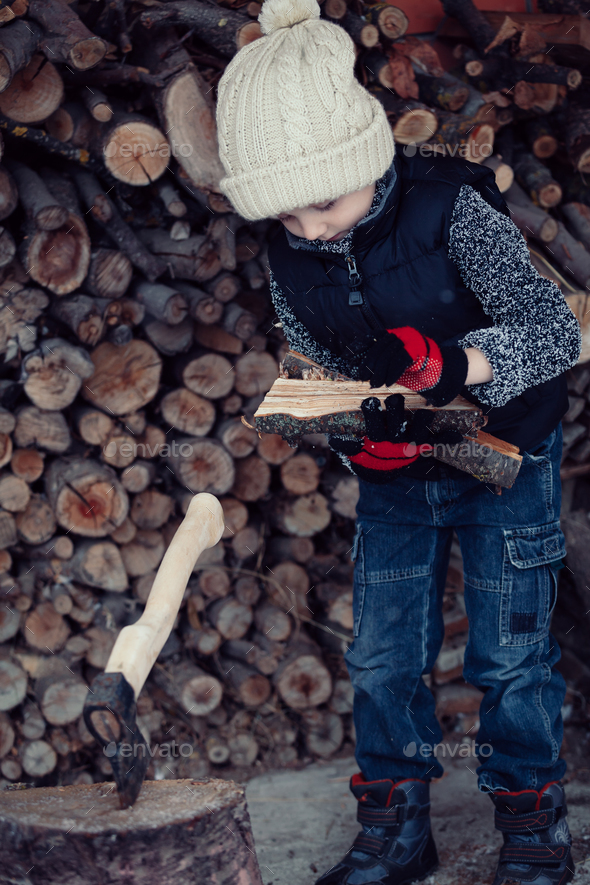 Little boy chopping firewood in the front yard at the day time. Stock Photo by altanaka