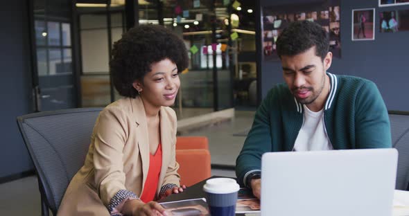 Diverse business people sitting using a laptop high fiving in a modern office alt