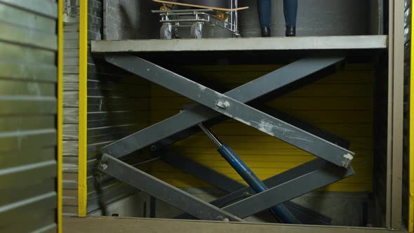 Scissor Lift Elevator Moving Down and Beautiful Smiling Woman Walking Away with Trolley alt