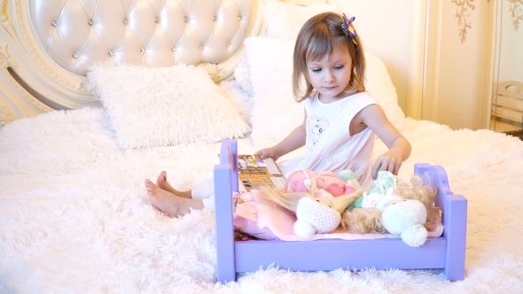 An Active Little Preschool Child, a Pretty Little Girl with a Blond Curly Hair, Plays with Her Dolls