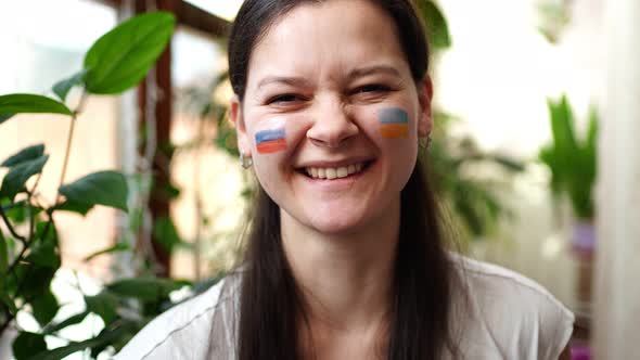 A Young RussianUkrainian Girl with the Flag of Ukraine and Russia on Her Face is Smiling alt