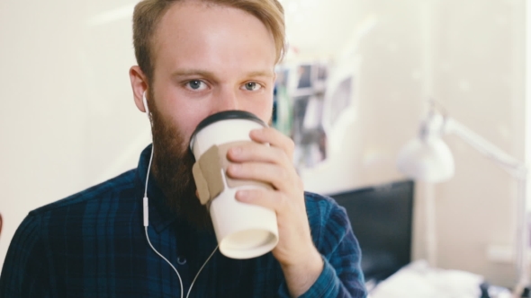 Hipster Drinking Coffee at Desk in Creative Office