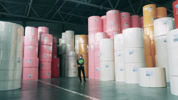 Female Worker Taking Notes in a Warehouse Full of Large Rolls of Paper alt