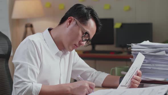 Close Up Of Asian Man Writing Something On Paper While Working With Documents At The Office alt