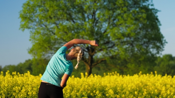 Fitness Training of an Gild at Open Air. Blooming Fresh Yellow Rapeseed Field with an Big Oak Tree alt