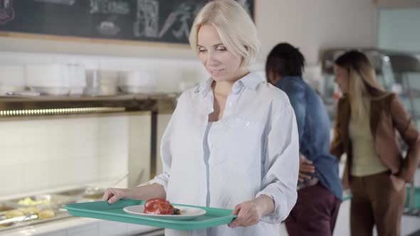 Charming Young Caucasian Blond Woman Holding Tray with Healthful Vegetarian Food Looking at Camera alt